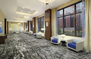A hotel room with a large window, multiple seating areas, and a chandelier.