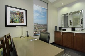 A conference room with a city view, a large framed abstract painting, and a modern kitchen area with a large mirror and cabinets. - Embassy Suites By Hilton Pittsburgh Downtown (Pittsburgh)