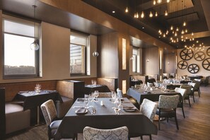 A restaurant with multiple dining tables set for guests, large windows, and a ceiling with hanging light fixtures. - Embassy Suites By Hilton Pittsburgh Downtown (Pittsburgh)
