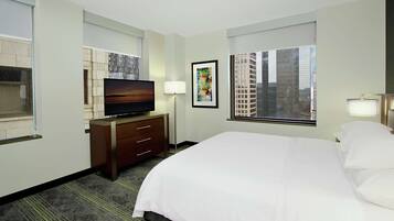 Habitación de hotel con una cama grande, un televisor de pantalla plana, un escritorio con cajones, una lámpara y una ventana con vista a la ciudad.
