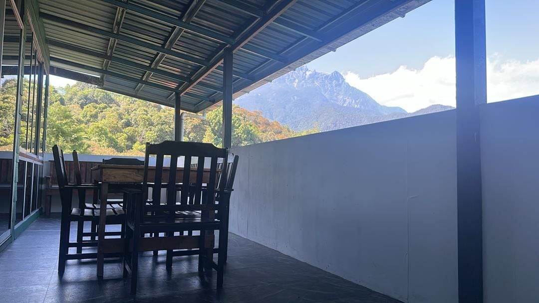 A covered outdoor seating area with a table and chairs, overlooking a mountainous landscape.
