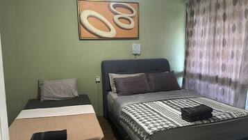 A room with two beds, one larger and one smaller, both with pillows and blankets.