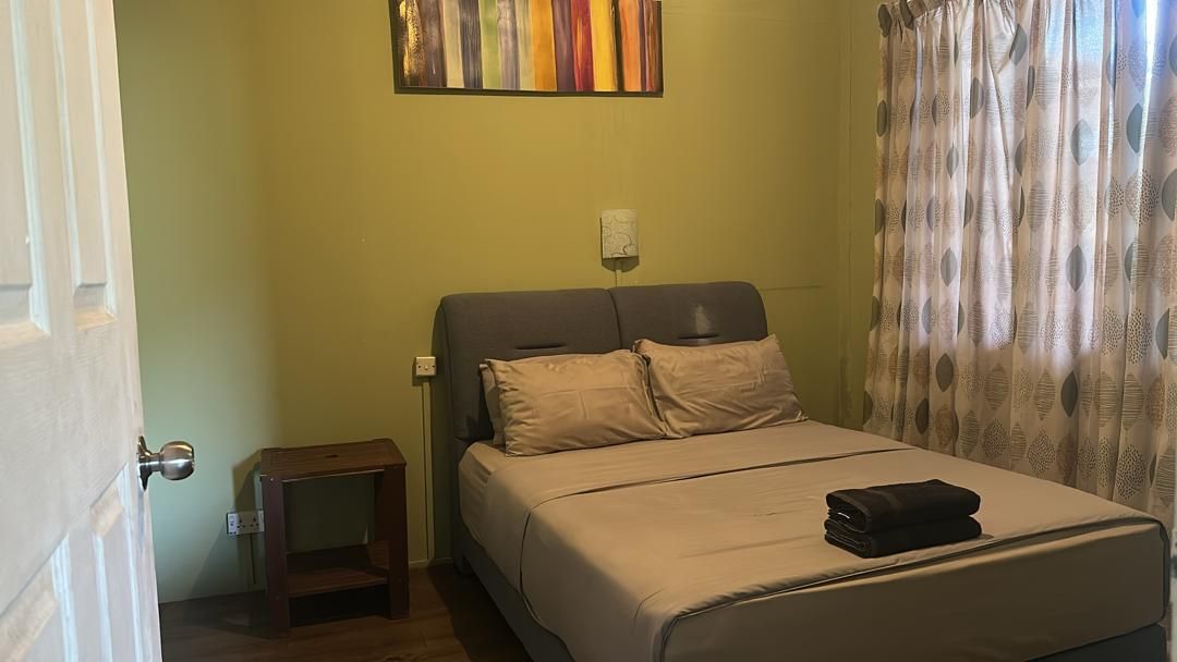 A bedroom with a bed, a nightstand, a wall-mounted light, and a window with curtains.
