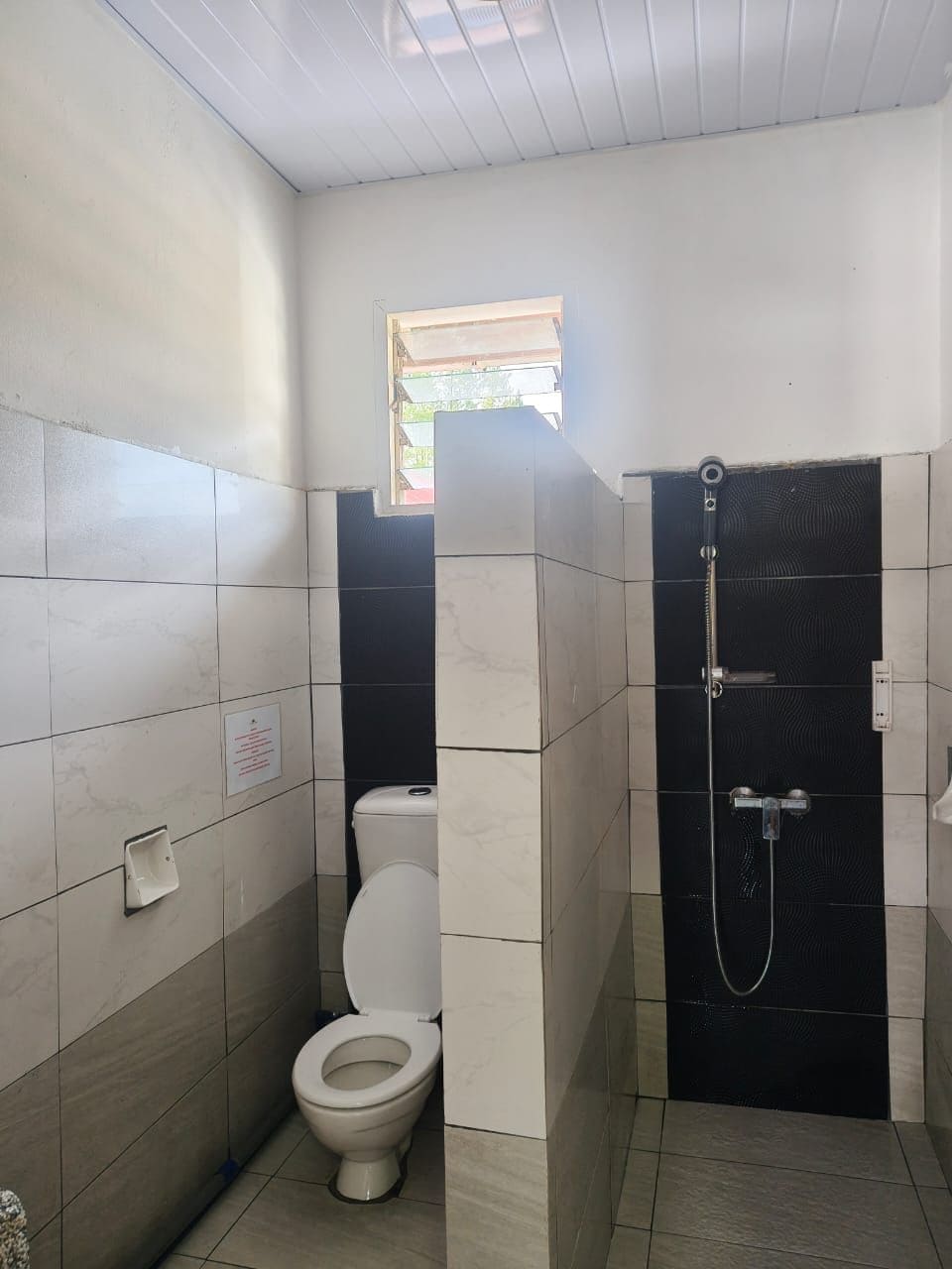 Ein Badezimmer mit Toilette, Dusche und einem kleinen Fenster.