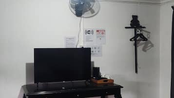 A room with a black desk, a wall-mounted fan, and a shelf with a hanging item.