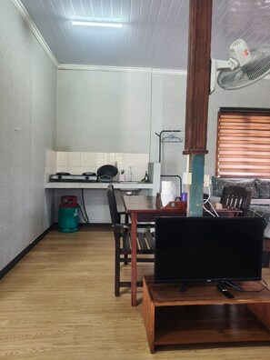 A compact living space with a kitchen area, a dining table, and a television on a wooden stand. - Ceaser's Place (Ranau)