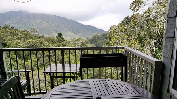 Una terraza de madera con una mesa y sillas, con vistas a un paisaje montañoso.