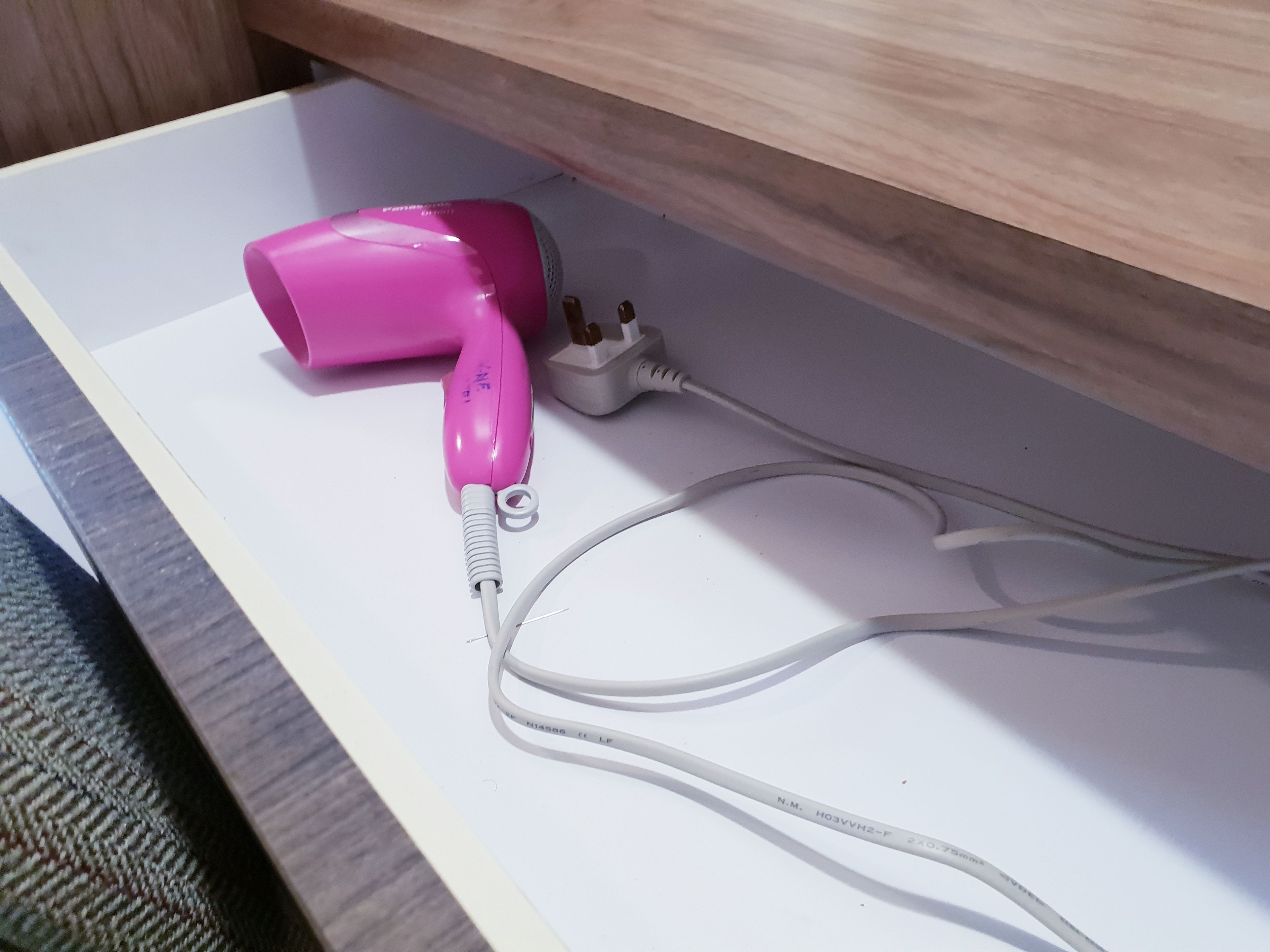 Un secador de pelo rosa sobre una superficie blanca, con cable de alimentación.