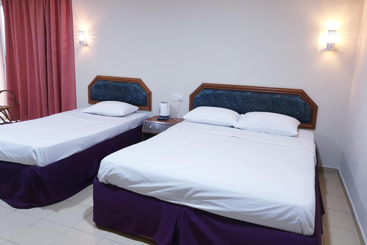 Two single beds with wooden headboards, white linens, and purple skirts. There is a nightstand with a lamp between the beds.
