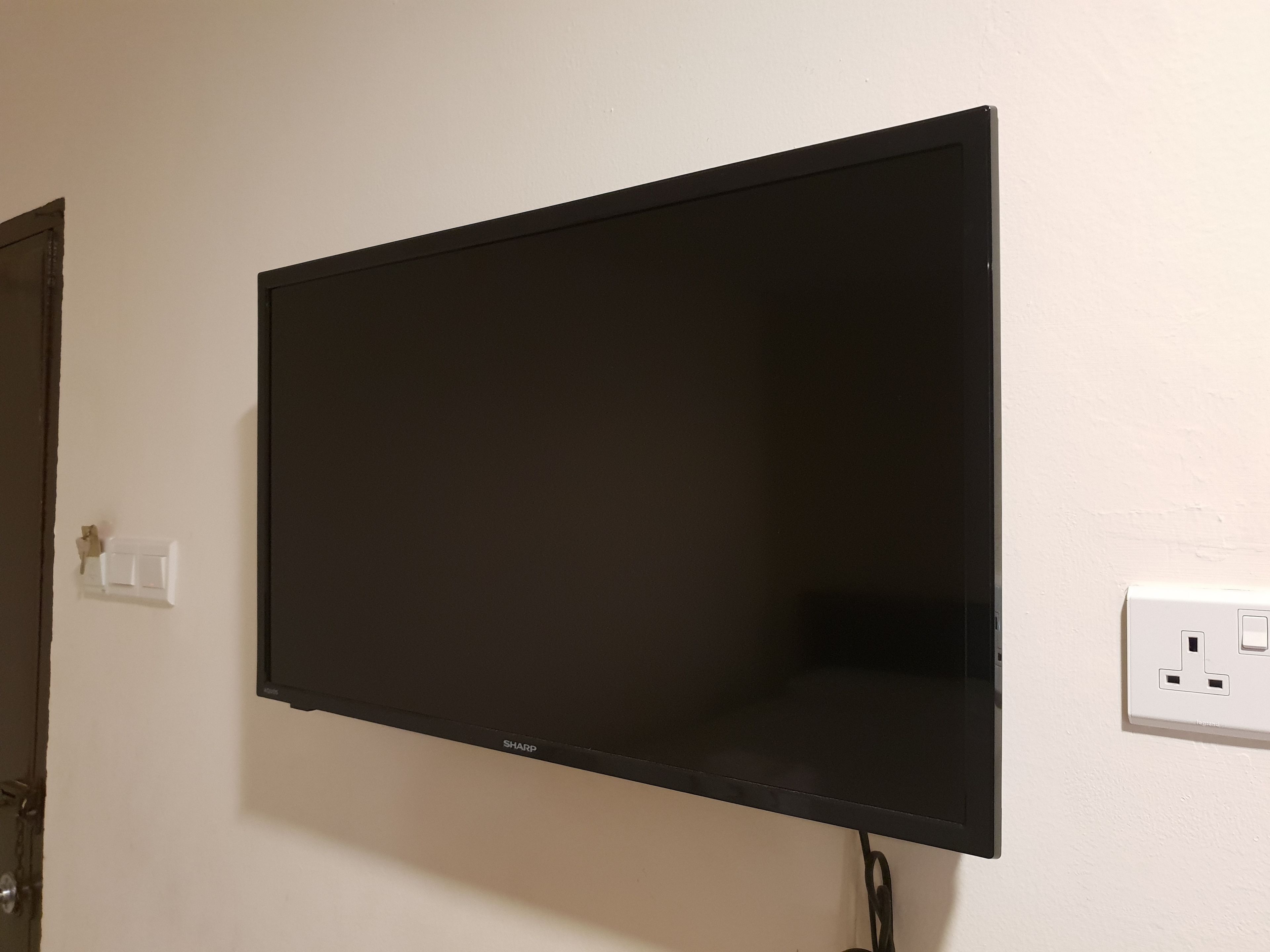 Un téléviseur à écran plat fixé au mur, avec une prise de courant sur le côté droit.