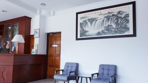 A reception area with a wooden desk, two blue chairs, a framed artwork of a waterfall, and a door with a sign. - Champcity Hotel (Kuantan)
