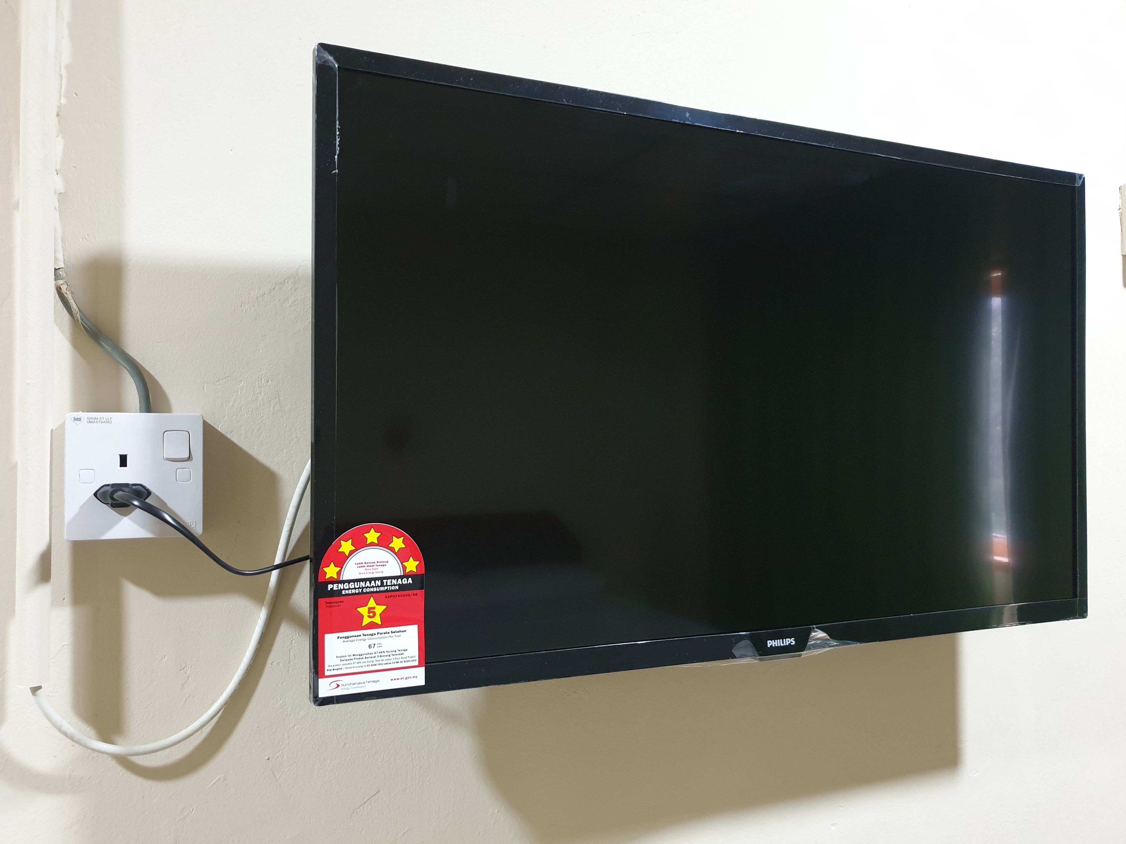 Televisor de pantalla plana montado en una pared, con el cable de alimentación conectado a una toma de corriente blanca.