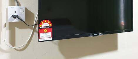 Televisor de pantalla plana montado en una pared, con el cable de alimentación conectado a una toma de corriente blanca.