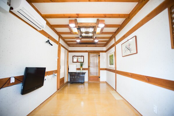 A hallway with wooden beams, a flat-screen TV mounted on the wall, a small table with a plant, and a framed picture on the wall.