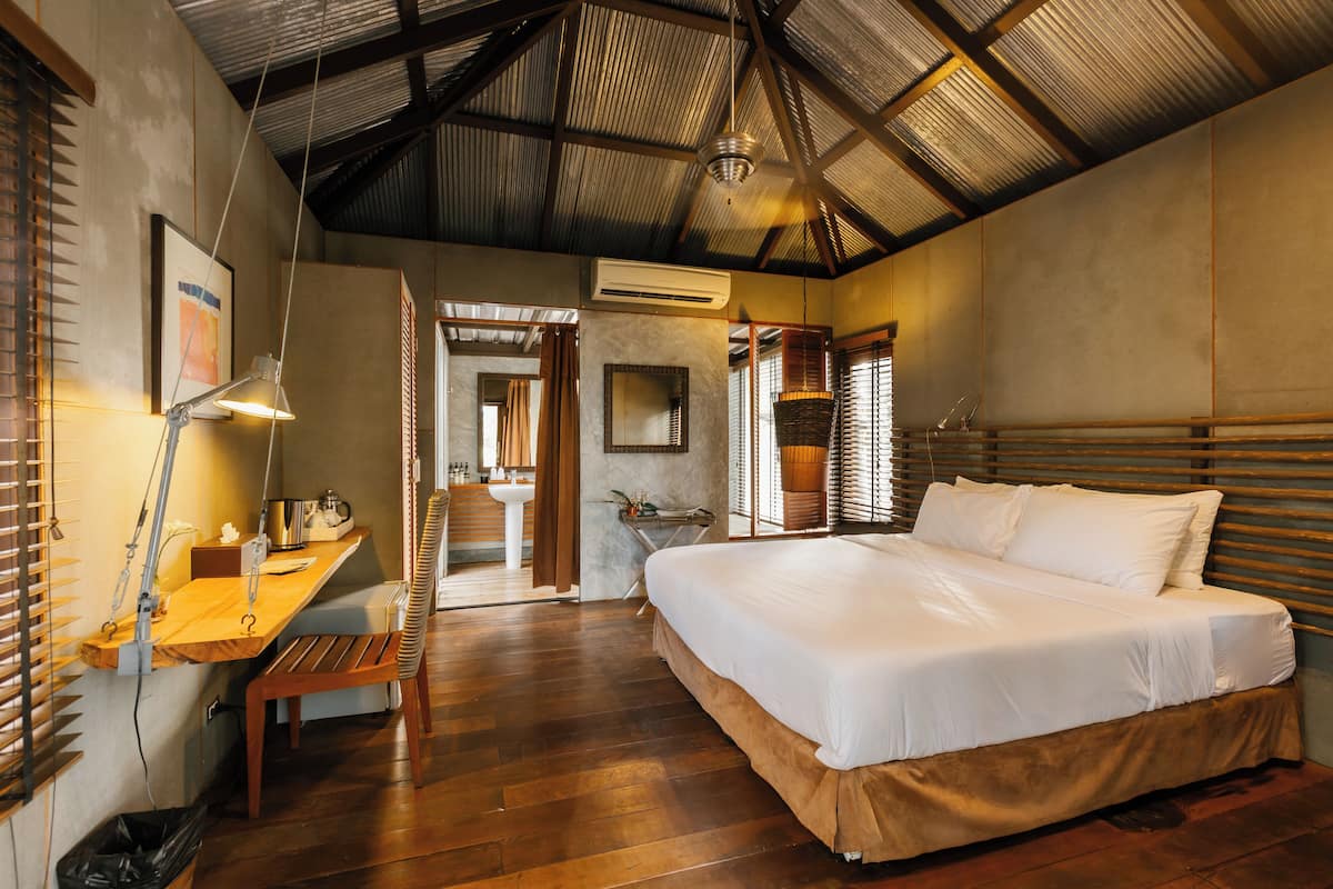 A bedroom with a large bed, wooden desk, and a bathroom visible through an open door.