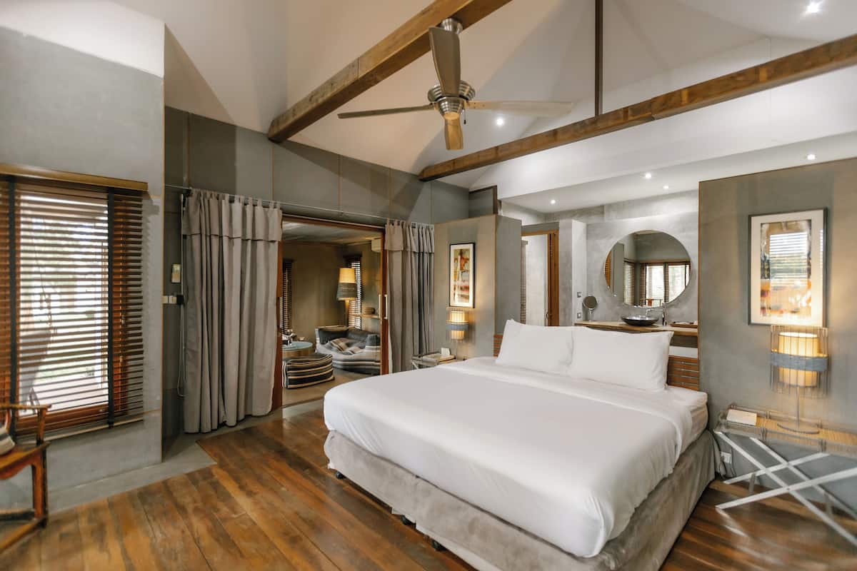 A spacious bedroom with a large bed, wooden flooring, a ceiling fan, and a walk-in closet with a mirror and seating area.