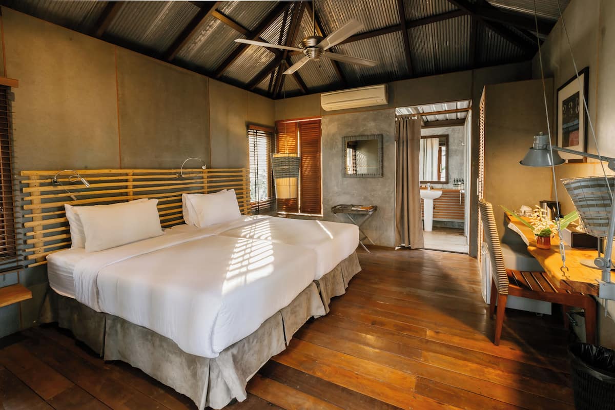 A spacious bedroom with a large bed, wooden flooring, a ceiling fan, and a view of the bathroom.