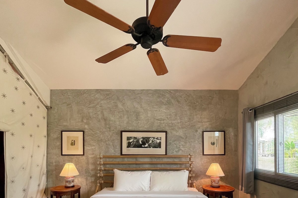 A bedroom with a large bed, two bedside lamps, a ceiling fan, and framed pictures on the wall.