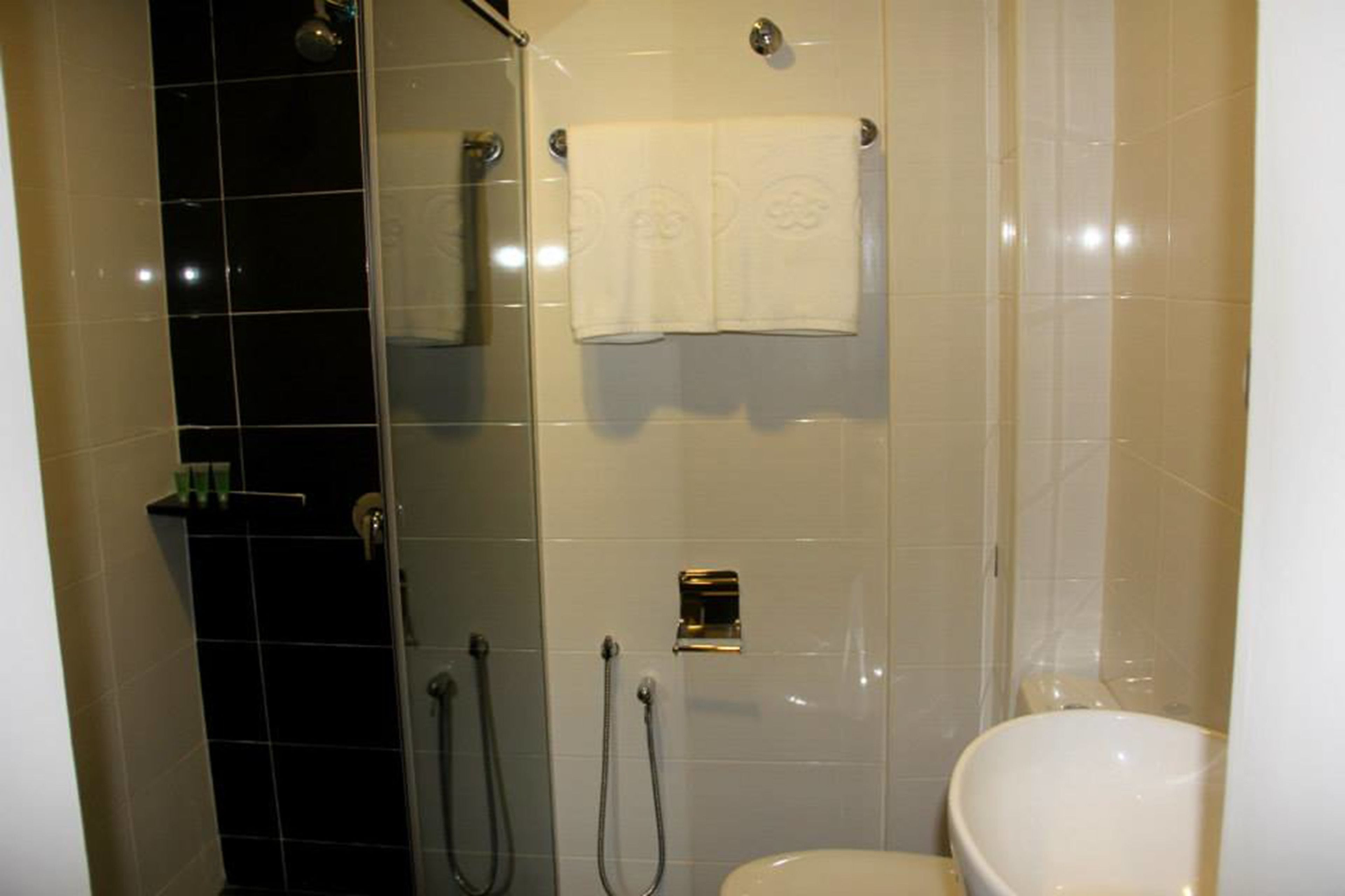 A bathroom with a glass-enclosed shower, a white toilet, and a towel rack with two towels.