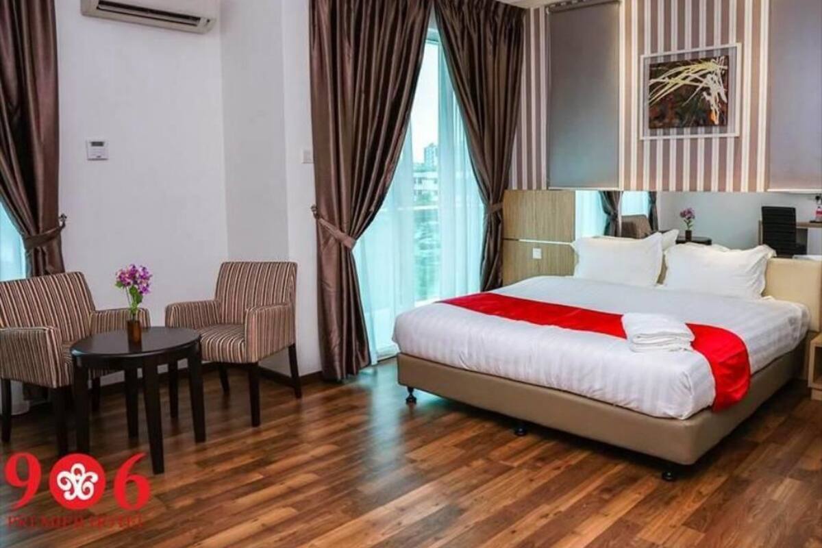 A hotel room with a large bed, a desk with two chairs, an air conditioning unit, and a window with curtains.