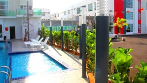 Une piscine avec des chaises longues, un escalier en colimaçon et un bâtiment moderne agrémenté de touches de rouge.