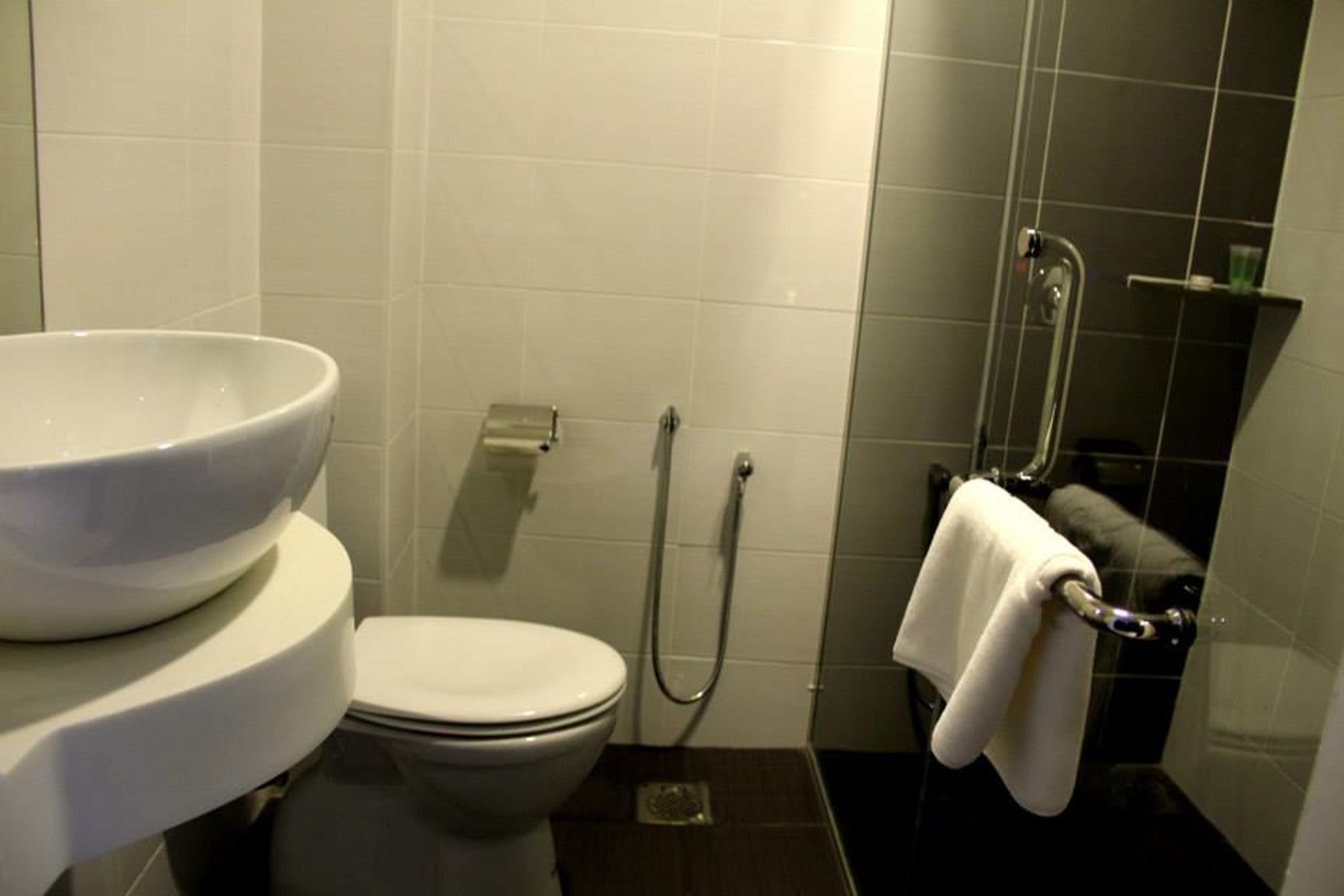 A bathroom with a white toilet, a large white basin, a shower with a handheld showerhead, and a towel rack with a towel.
