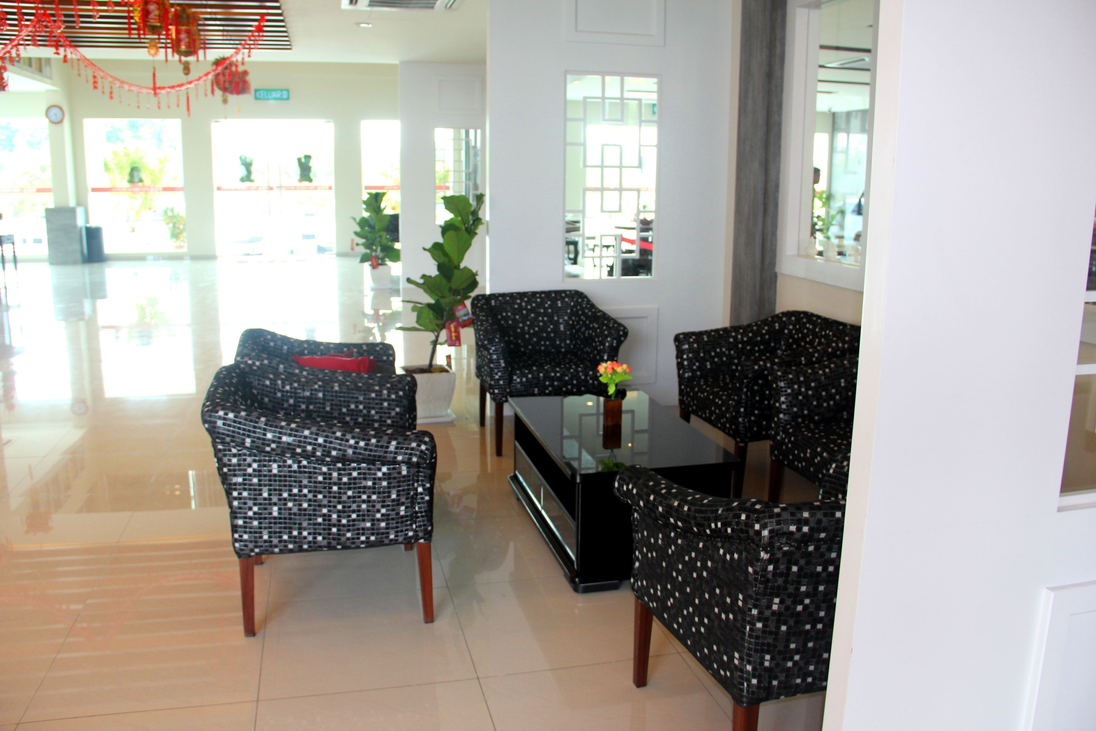 A modern hotel lobby with a seating area featuring black chairs with a white pattern, a glass coffee table, and a potted plant.
