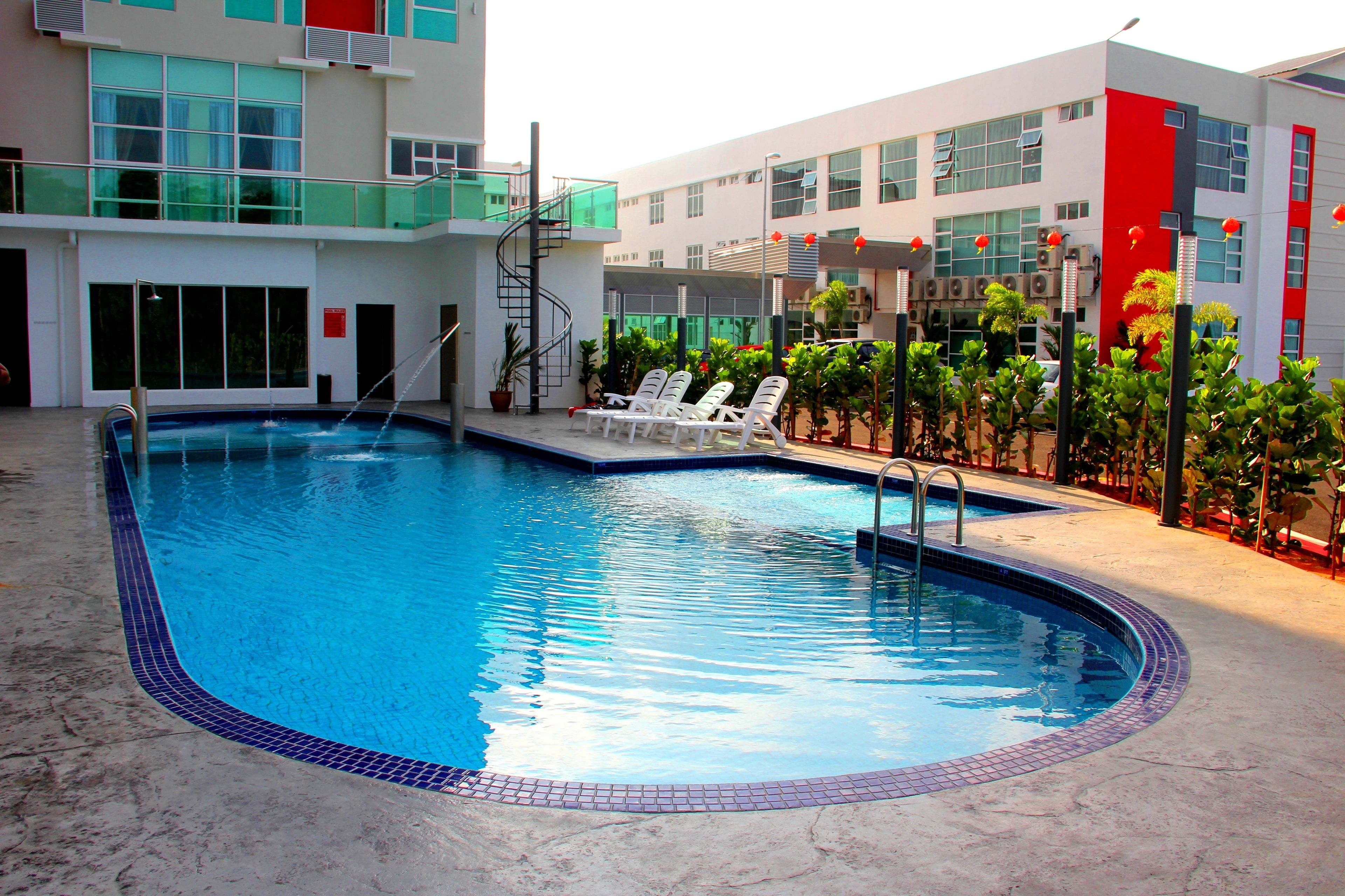 A swimming pool with lounge chairs, a spiral staircase, and a modern building with large windows and balconies.