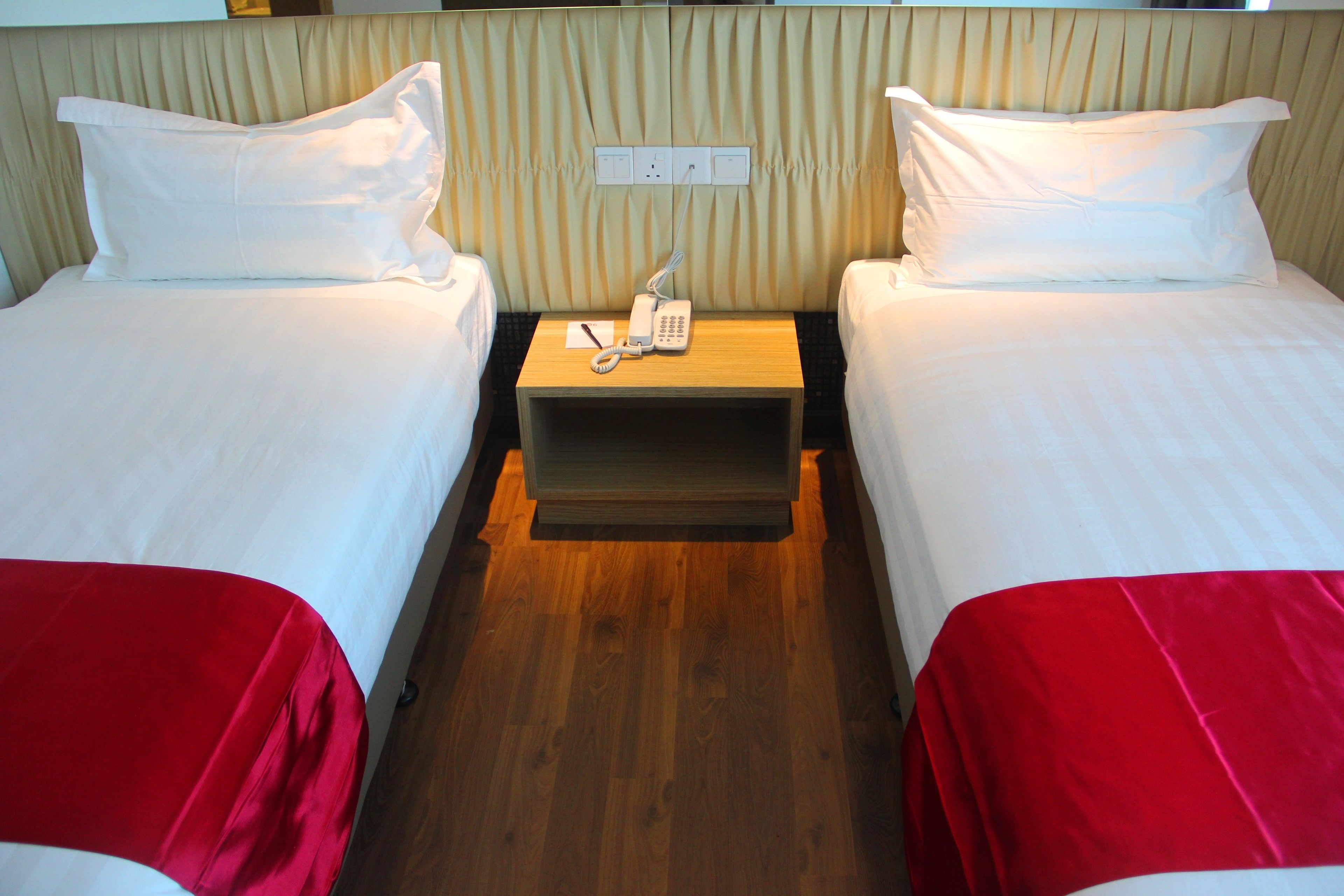 A hotel room with two beds, each with white linens and red bedspreads. There is a wooden nightstand between the beds with a telephone and a notepad.