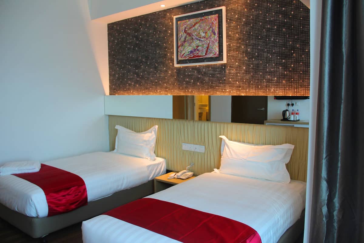 Two single beds with white linens and red accents, a bedside telephone, and a wall-mounted artwork above the beds.