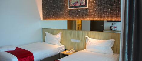 Two single beds with white linens and red accents, a bedside telephone, and a wall-mounted artwork above the beds.