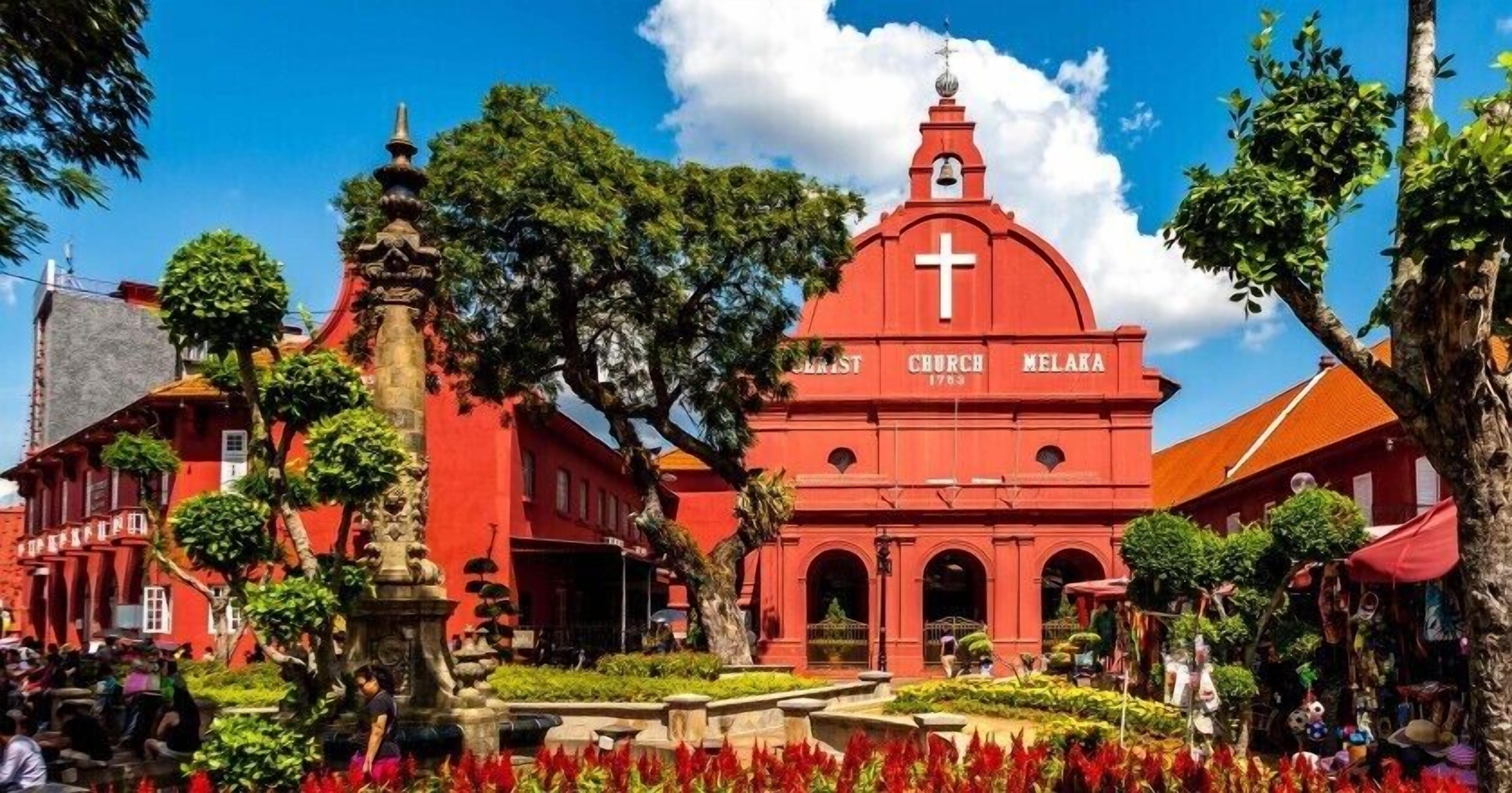 Una iglesia roja con una cruz en la parte superior, rodeada de árboles y un jardín.