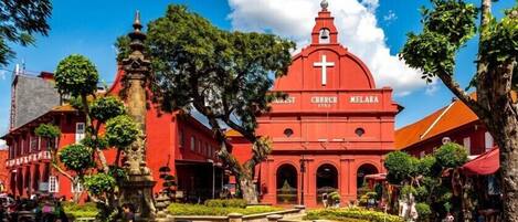 Una iglesia roja con una cruz en la parte superior, rodeada de árboles y un jardín.