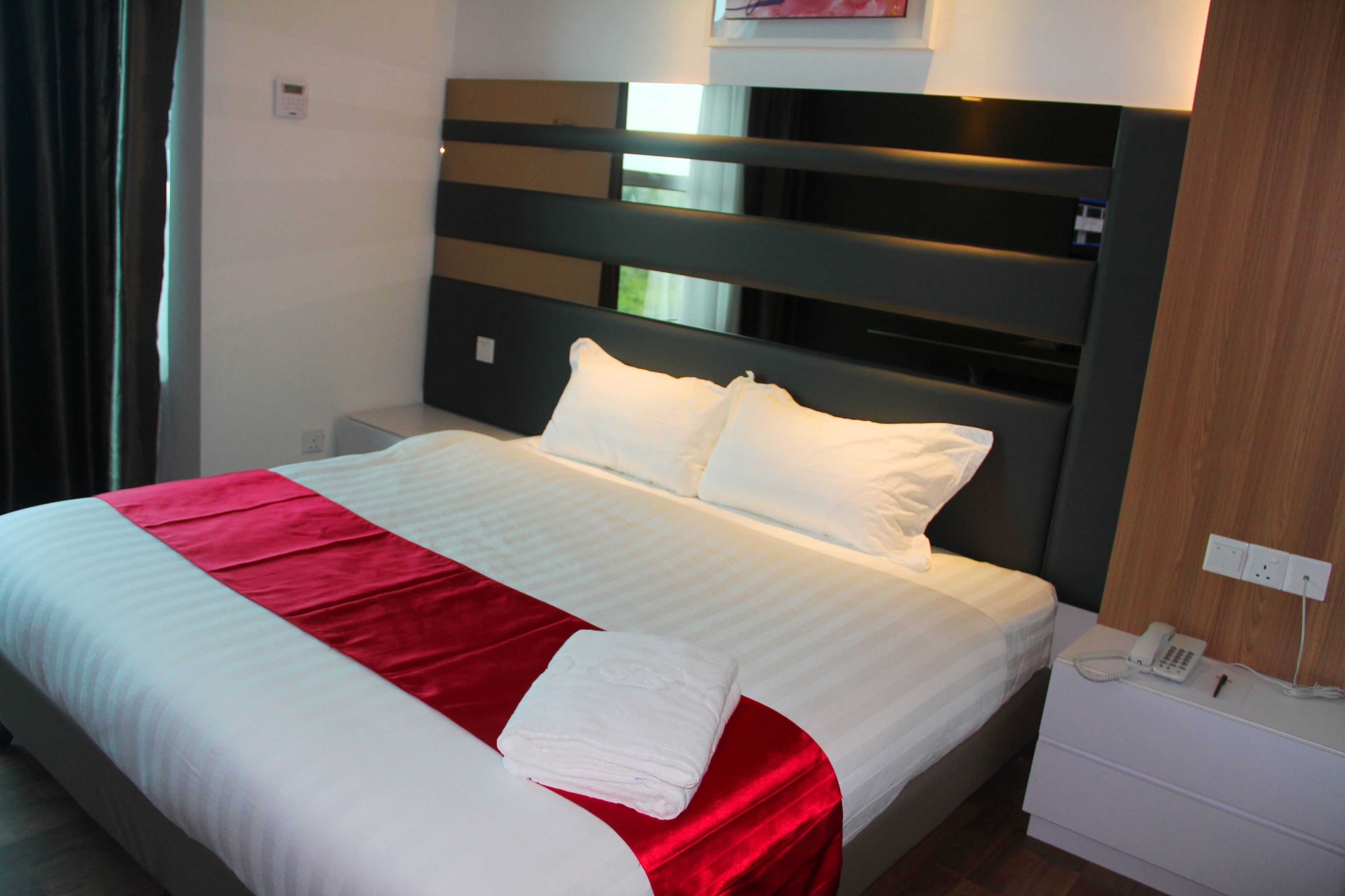 A neatly made bed with white and red bedding, a bedside phone, and a nightstand.