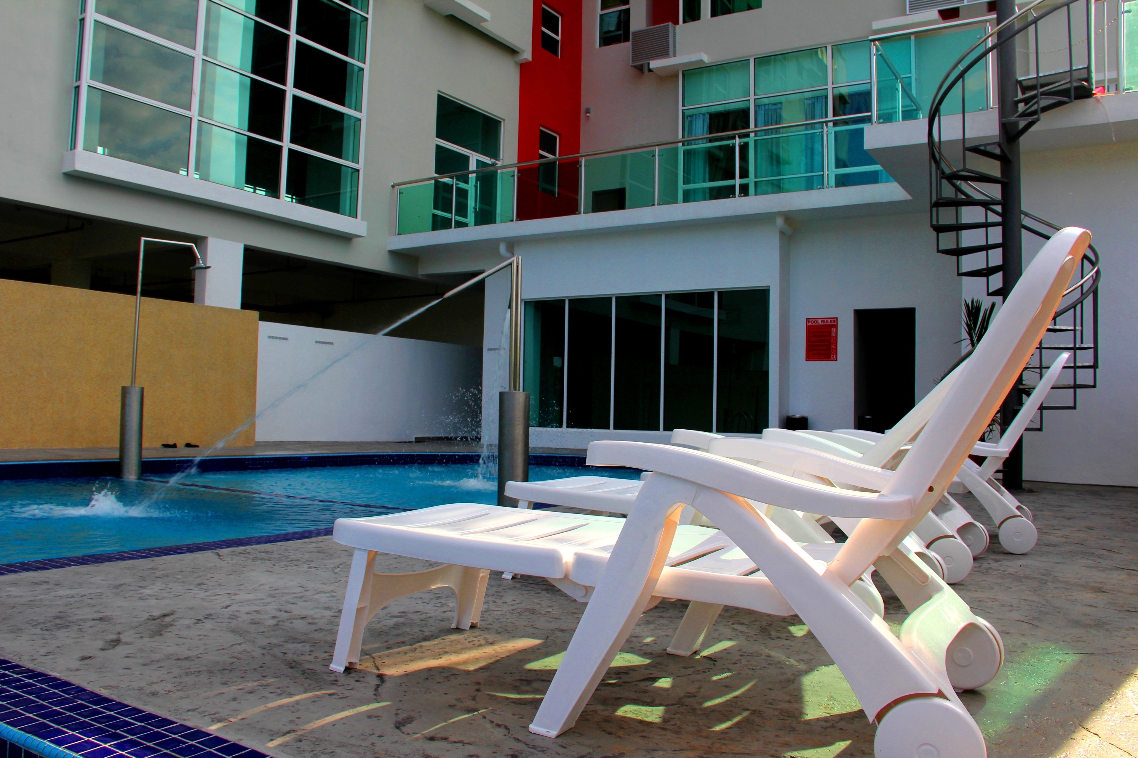 A swimming pool with lounge chairs, a water feature, and a multi-level building with balconies.