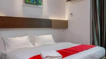 A hotel room with a large bed, white bedding, a red accent, an air conditioning unit, and a painting on the wall.
