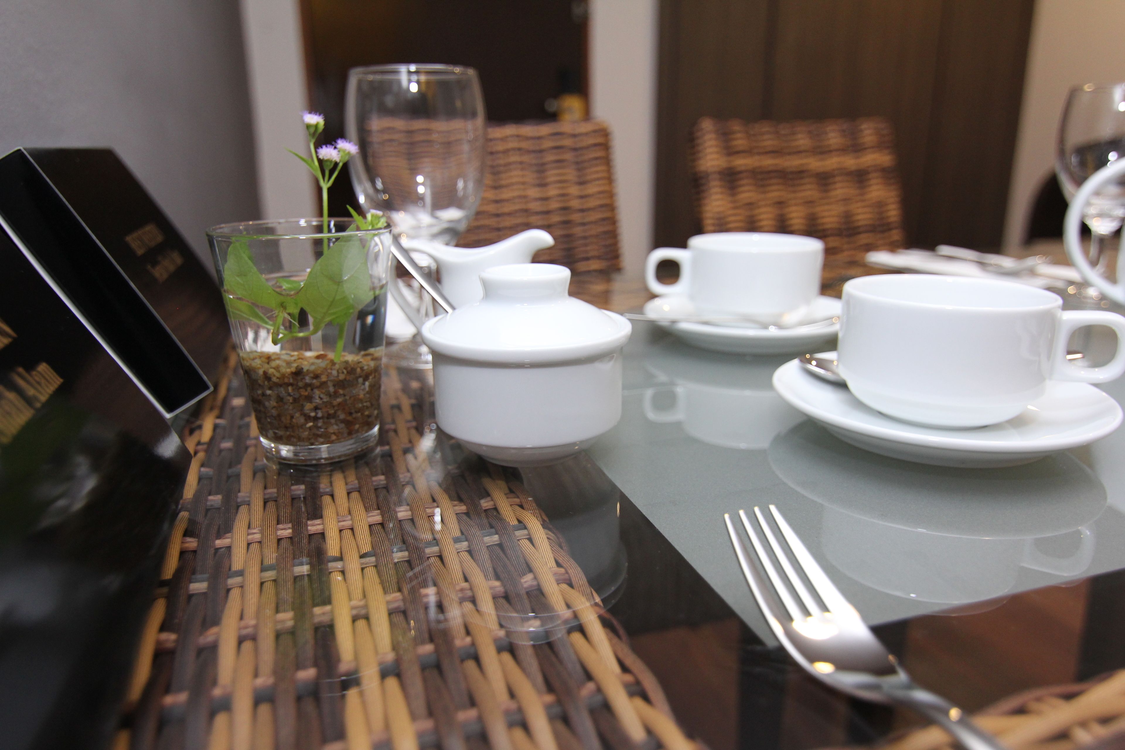 A dining table set with white cups, saucers, a teapot, and a small vase with a plant.