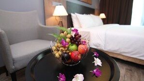 Quarto de hotel com uma cama, um sofá, uma mesa com uma fruteira e uma luminária.