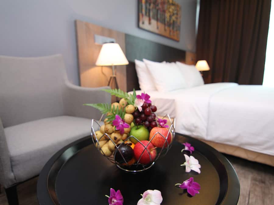 Una habitación de hotel con una cama, un sofá, una mesa con frutero y una lámpara.