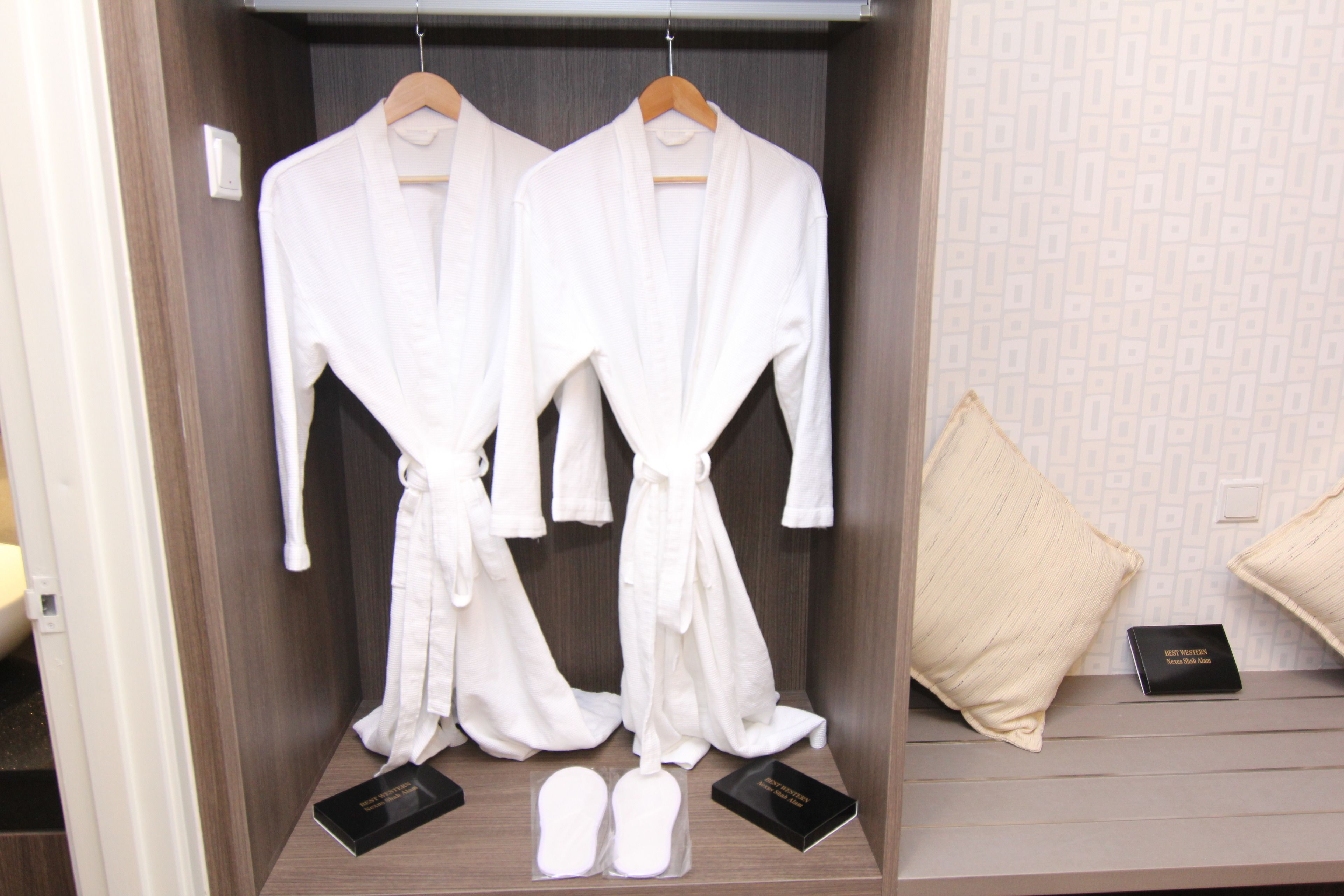 Une chambre d’hôtel avec une armoire en bois contenant deux peignoirs blancs, une paire de chaussons et un oreiller.