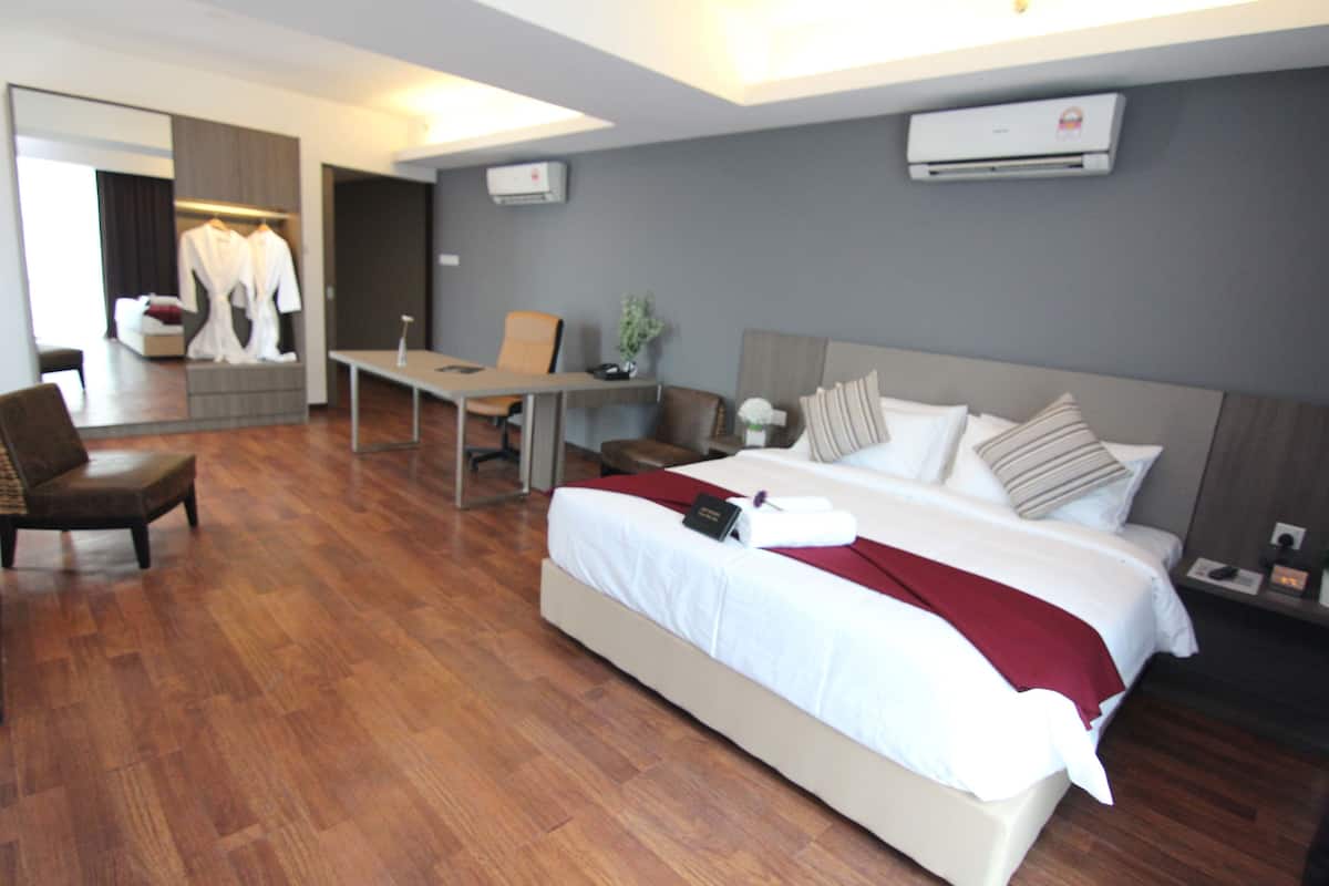 A modern hotel room with a large bed, a desk, and a chair. There is a mirror, an air conditioning unit, and a small table with a plant.