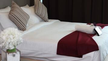 A neatly made bed with white and maroon bedding, striped pillows, and a small vase with white flowers on a bedside table.