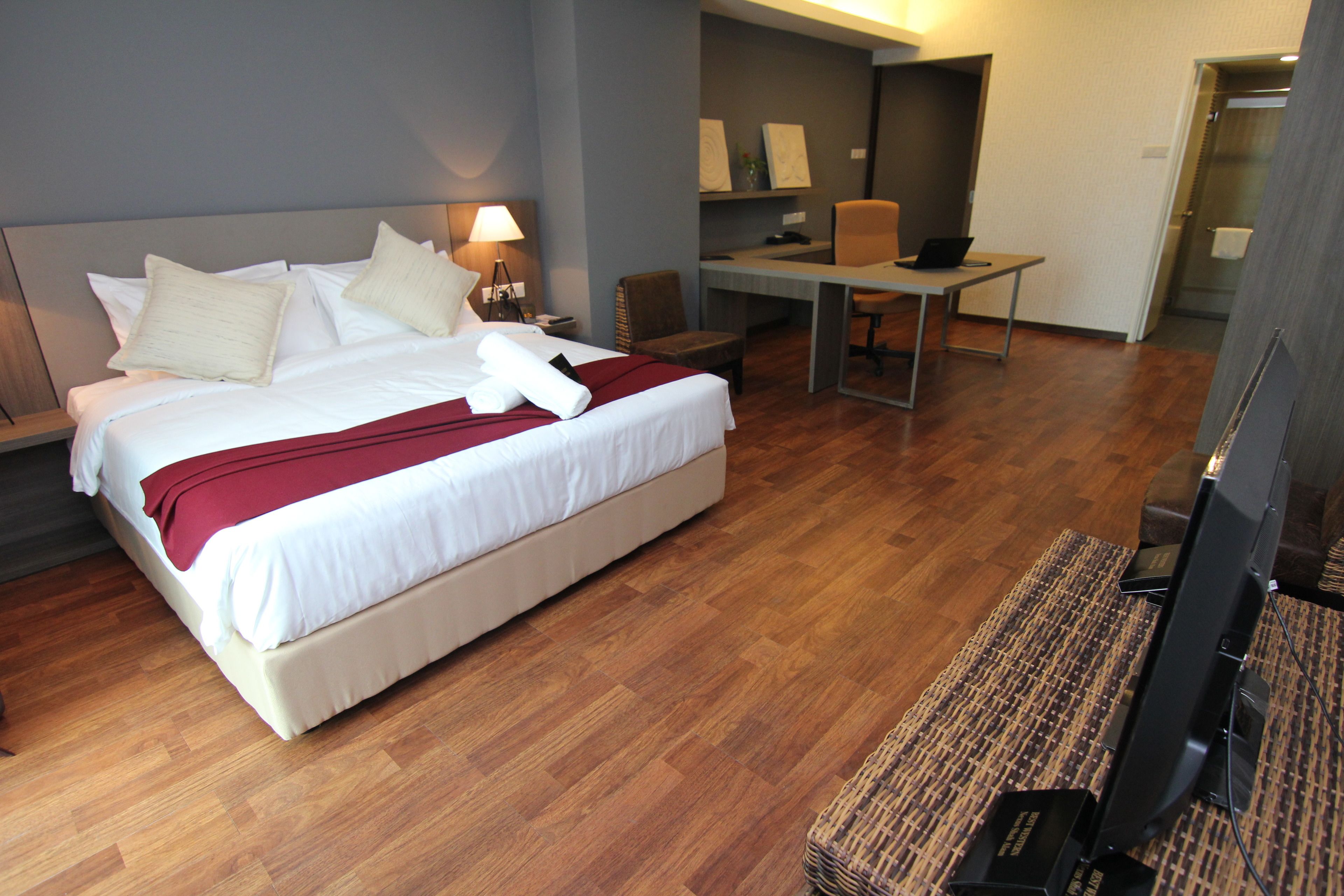 A hotel room with a large bed, a desk, a chair, and a television.