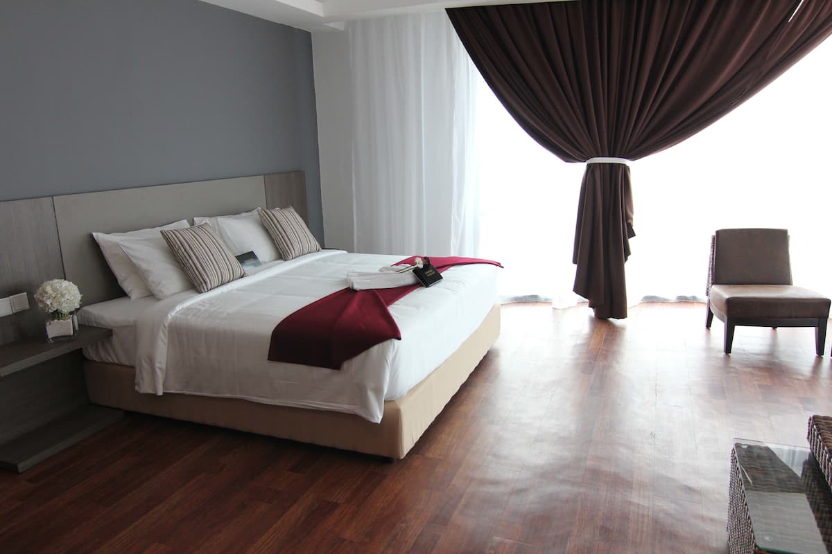A modern hotel room with a large bed, a bedside table with a vase of flowers, a chair, and a view of the outdoors.