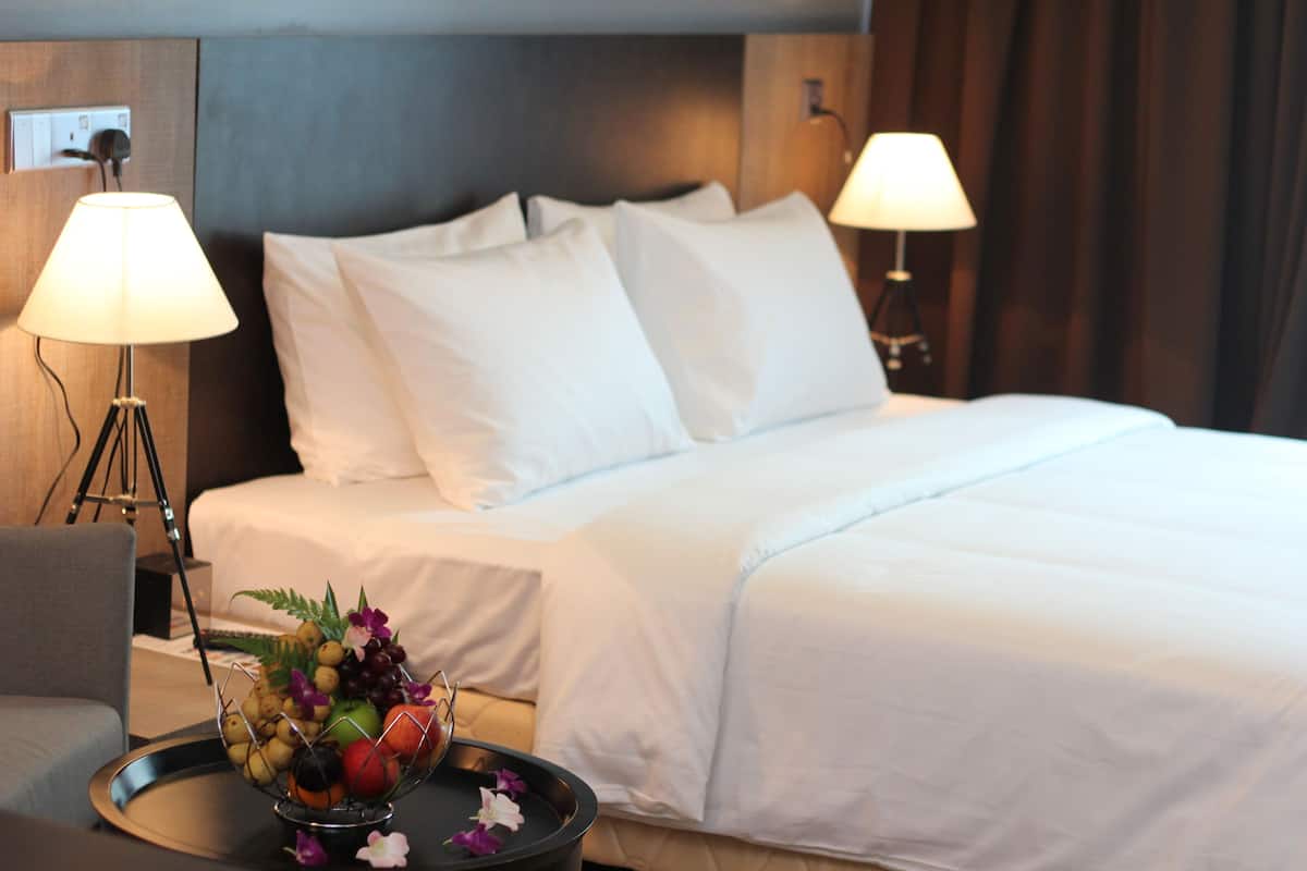 A hotel room with a neatly made bed, two bedside lamps, and a fruit bowl on a side table.