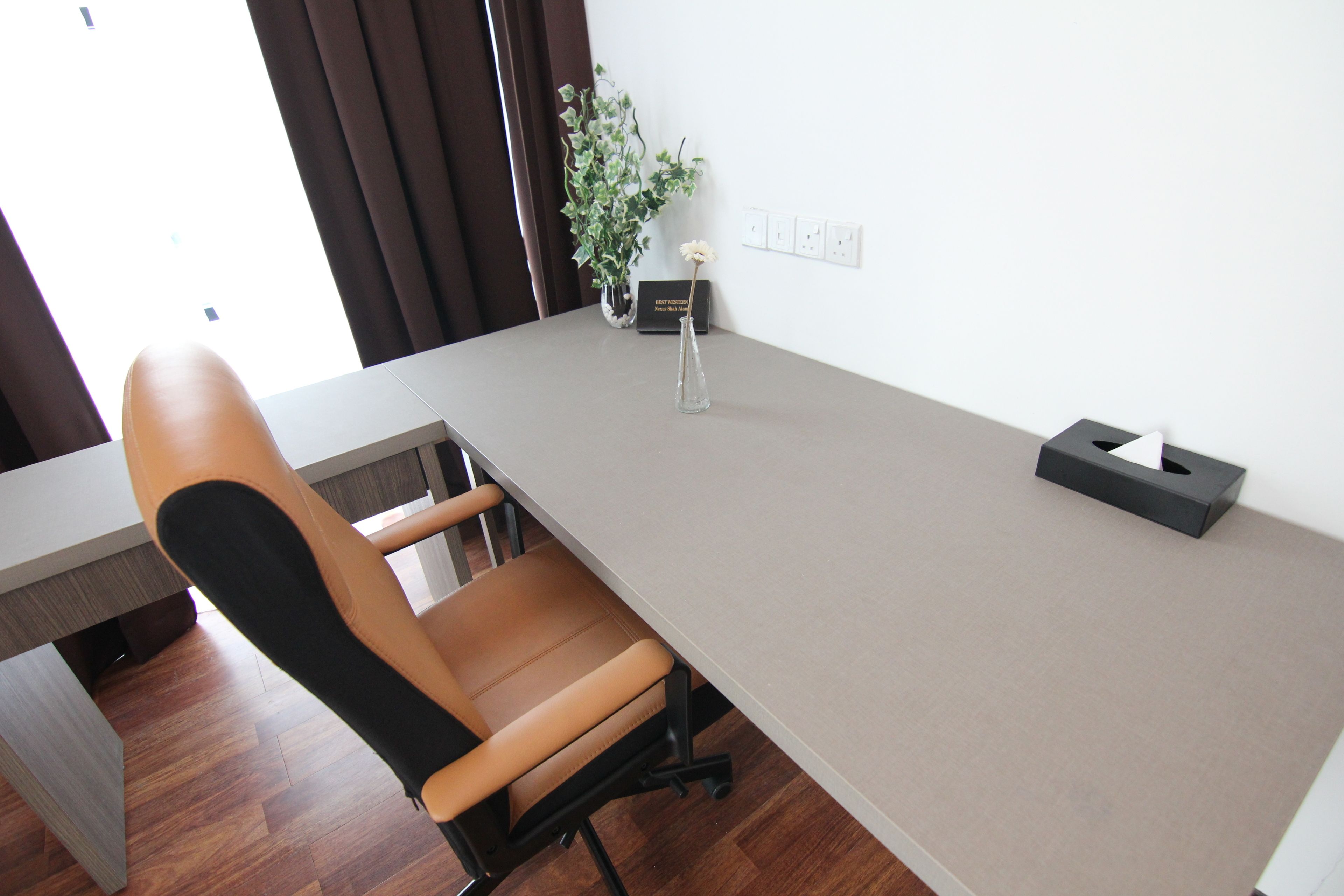A modern office space with a long table, a single office chair, a potted plant, and a tissue box on the table.
