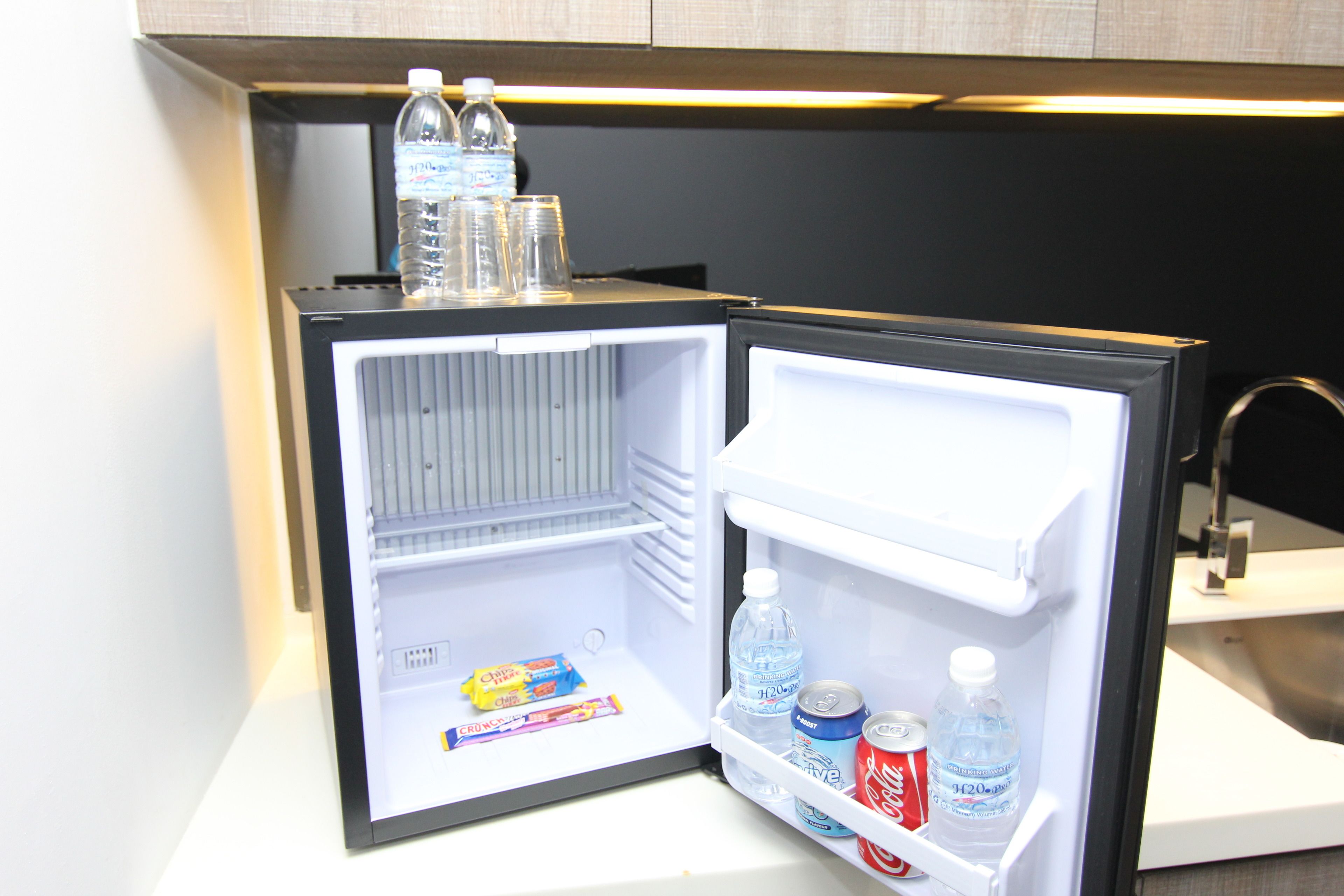 Ein offener Kühlschrank mit Wasserflaschen, einer Cola und einer Tüte Snacks.
