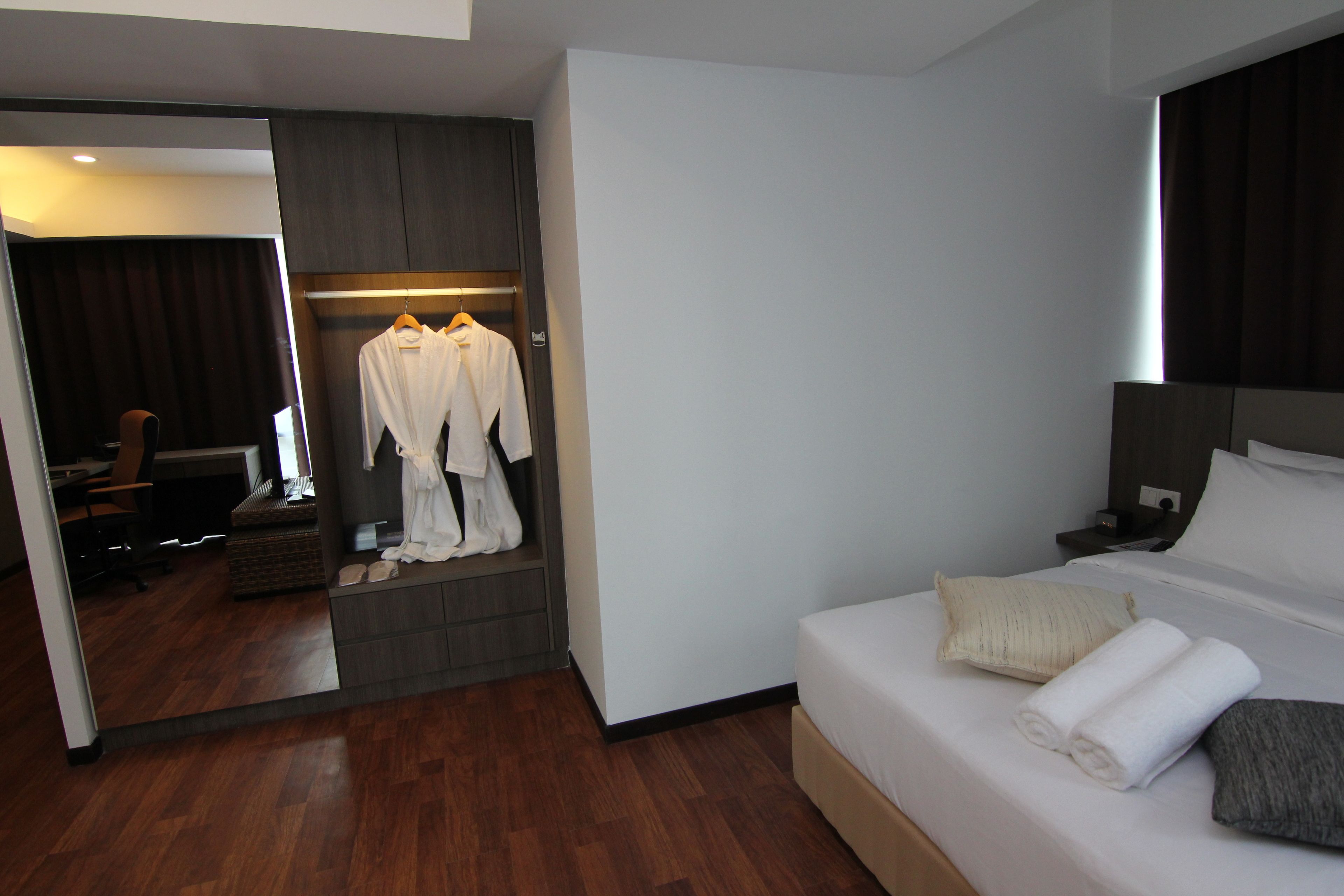 Quarto de hotel com cama, mesa de cabeceira, espelho, guarda-roupa e área de estar com uma cadeira e mesa.