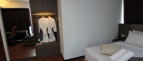 Quarto de hotel com cama, mesa de cabeceira, espelho, guarda-roupa e área de estar com uma cadeira e mesa.