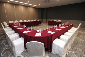 Una sala de conferencias con una larga mesa, sillas blancas y botellas de agua.